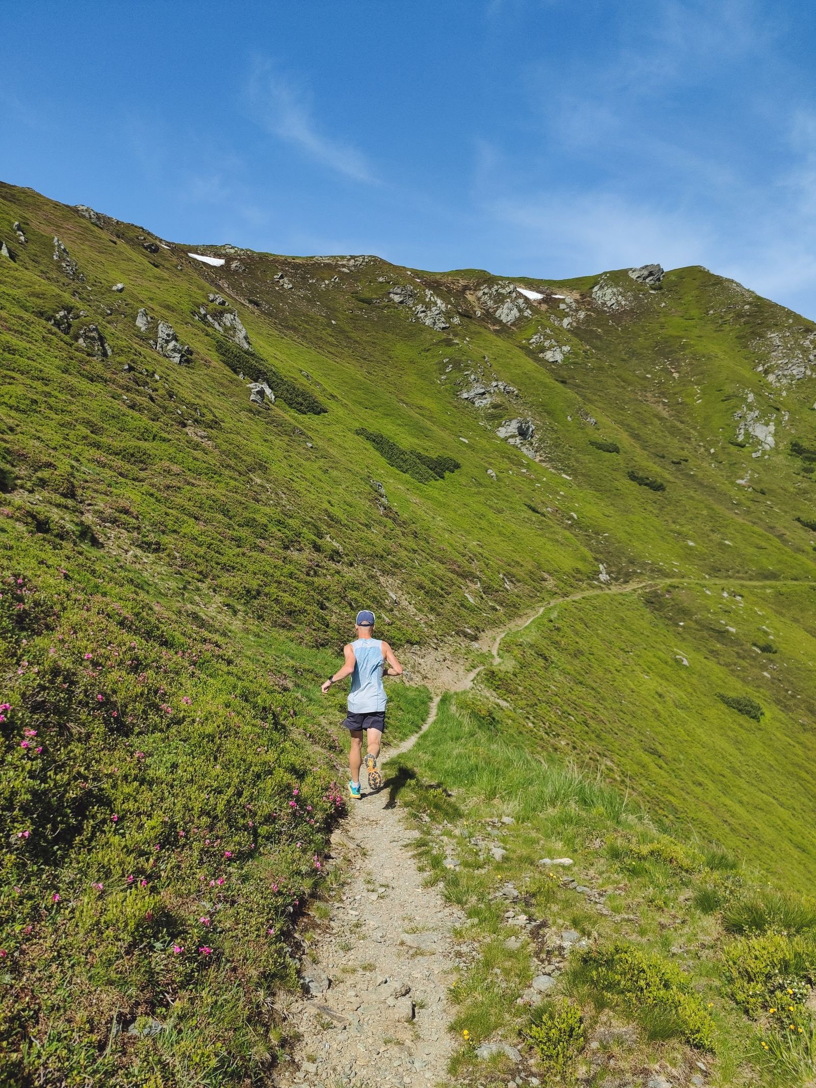 A runner following a narrow stony path across a steep green fellside under a blue sky